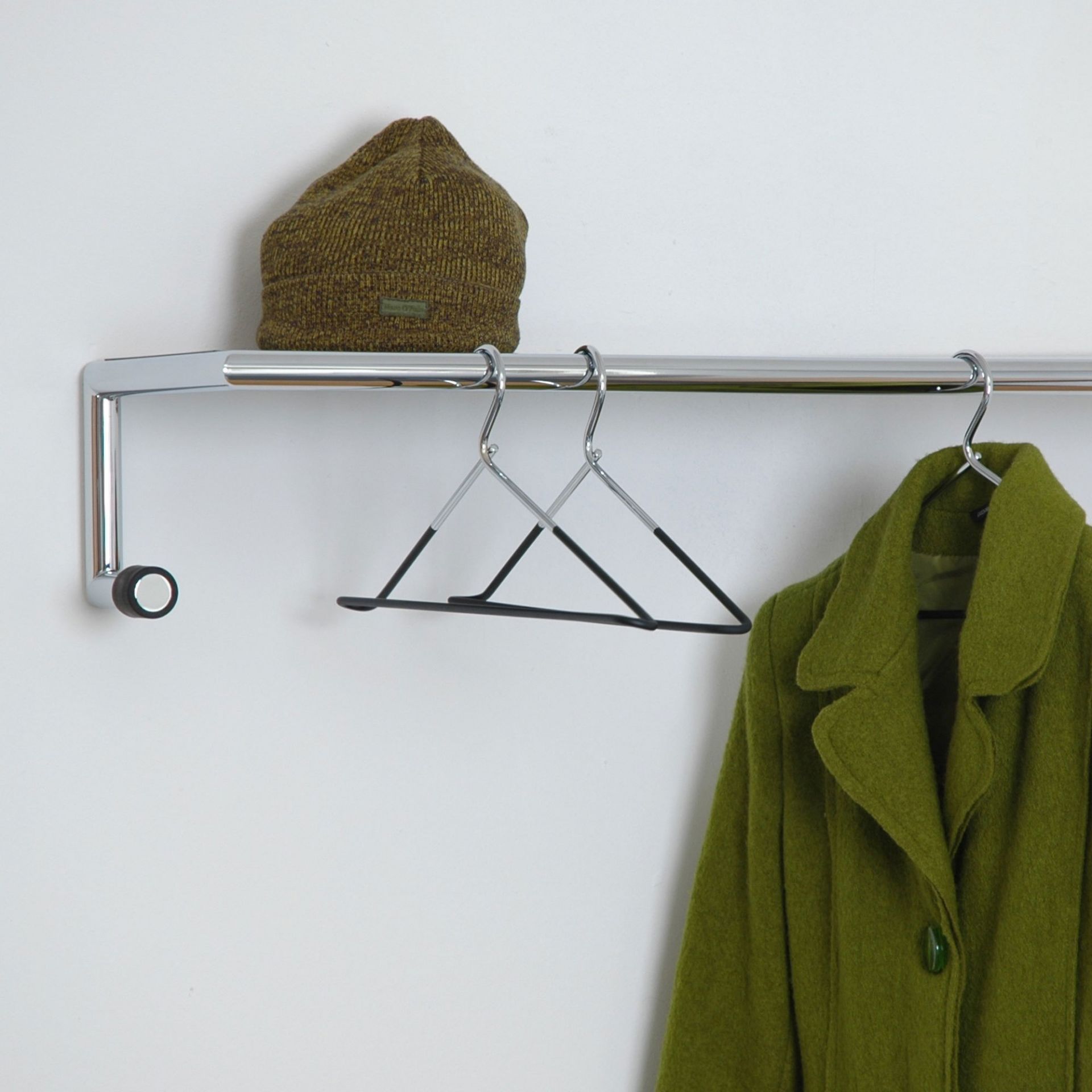 Link Wall Wandgarderobe von Mox mit Hut, Kleiderbügel und grünem Mantel an weißer Wand.
