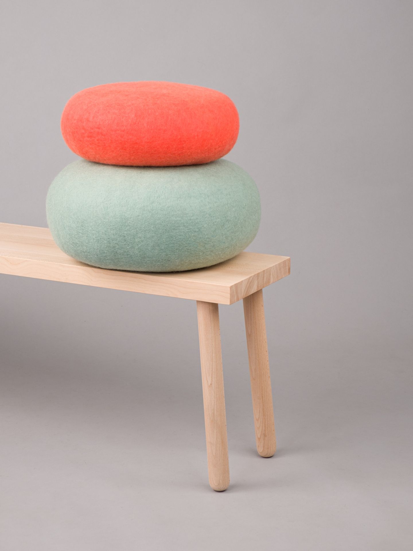 Filz Colour Pouf Hocker von myfelt, gestapelt auf einer Holzbank, rot und mintgrün.