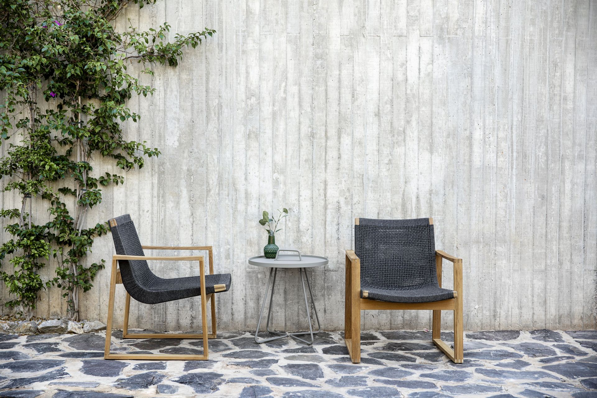 Zwei Cane-Line Loungesessel aus Teakholz und grauem Geflecht mit Beistelltisch im Garten.