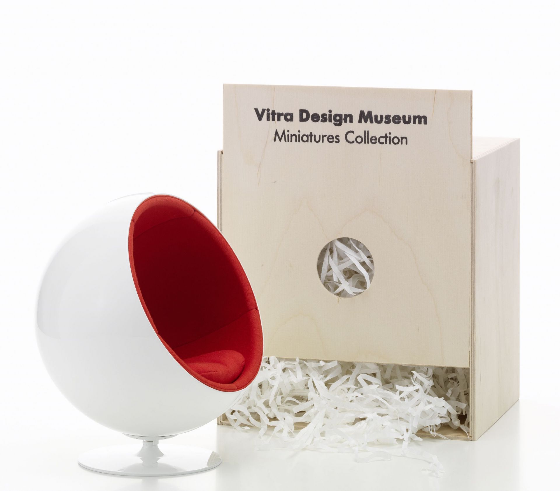 Miniatur des Ball Chair von Vitra, weiß mit rotem Innenraum, neben einer Holzkiste.