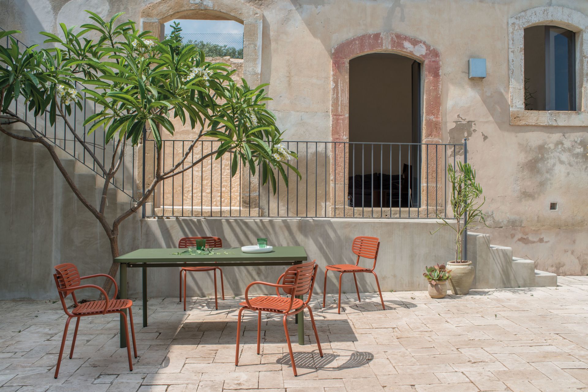 Emu Mom Armlehnenstuhl in Terrakotta und grüner Tisch im mediterranen Außenbereich. Gartenmöbel für Terrasse.