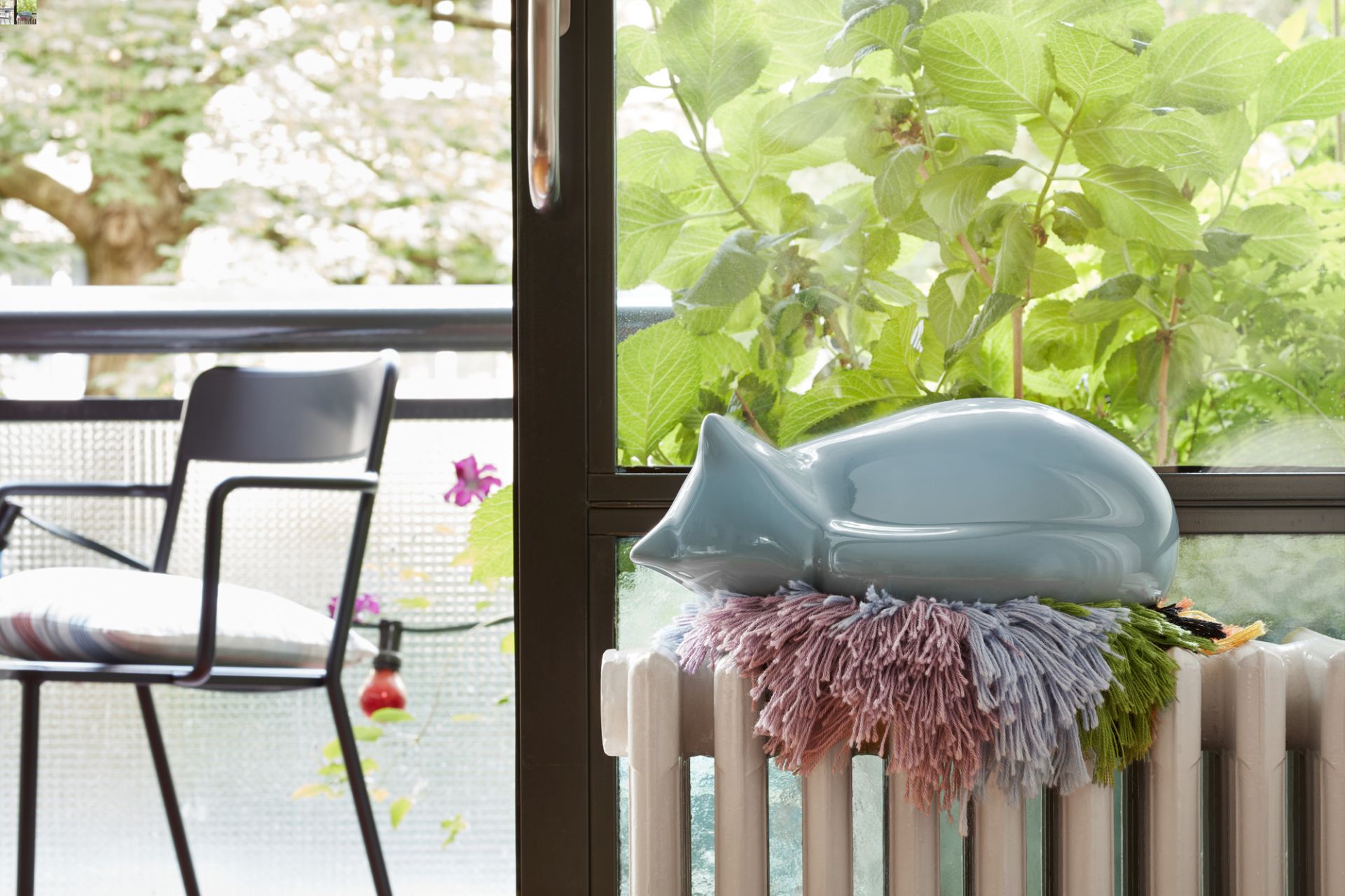 Hellblaue Vitra Katze Figur, liegend auf einem Heizkörper mit farbiger Wolle. Dekorative Wohnaccessoires für Katzenliebhaber.