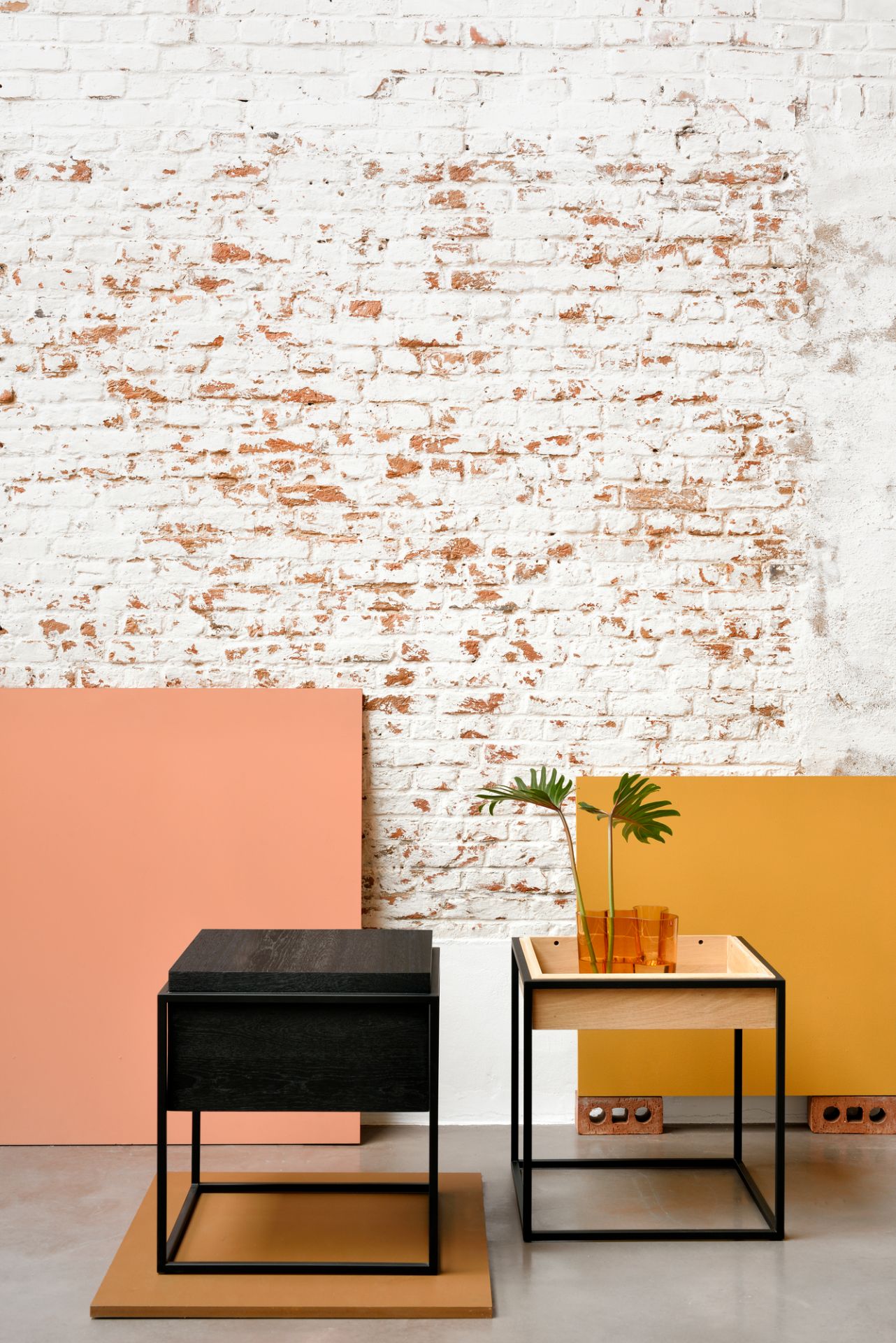 Schwarzer Ethnicraft Monolit Beistelltisch aus Eiche neben einem hellen Eichenholz Beistelltisch mit Pflanze.