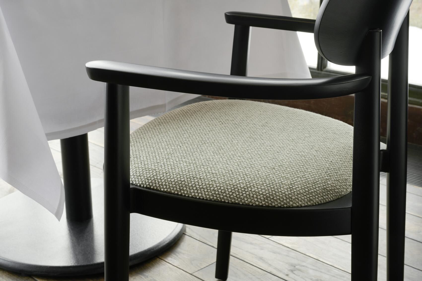 Detailaufnahme: Schwarzer 118 SPFV Thonet Holzstuhl mit Armlehnen und hellgrauem Stoffbezug.