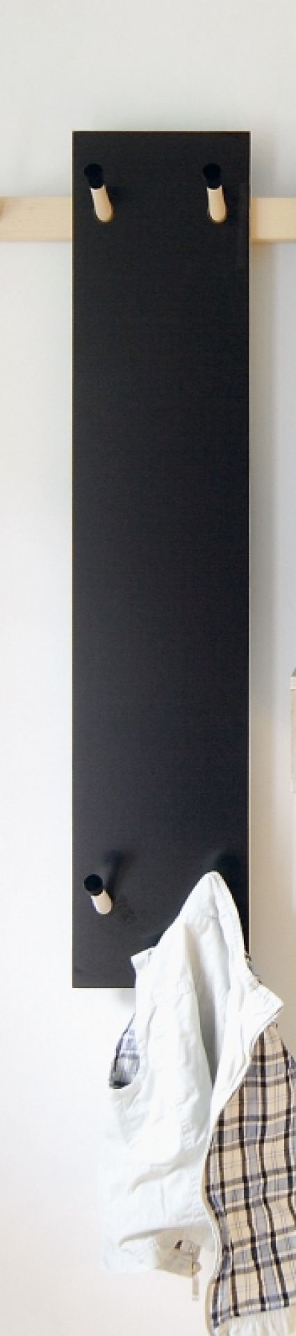 Schwarze Kindergarderobe von Moormann mit Holzhaken und hängender Kinderkleidung an einer weißen Wand.