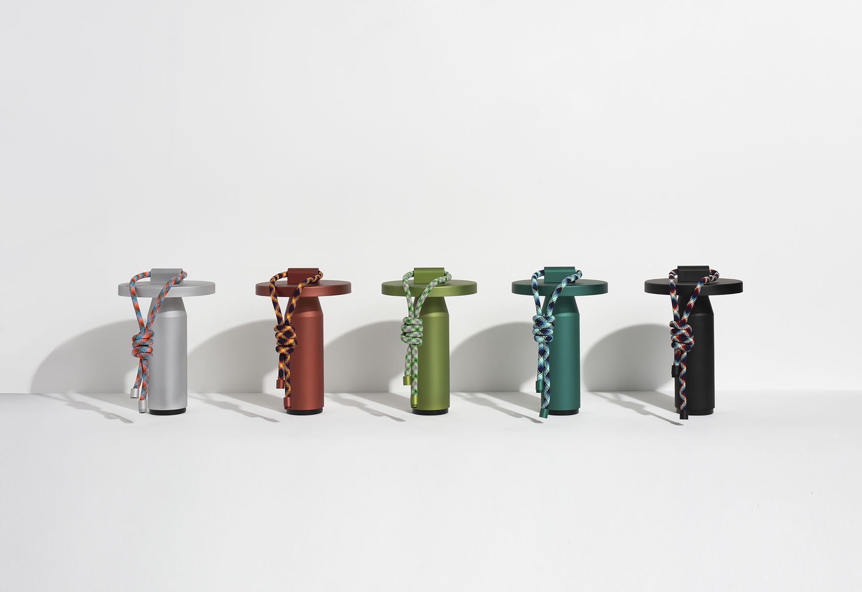 Fünf Quasar Nomad Lampen in Grau, Braun, Hellgrün, Grün und Schwarz mit farbigen Kordeln.