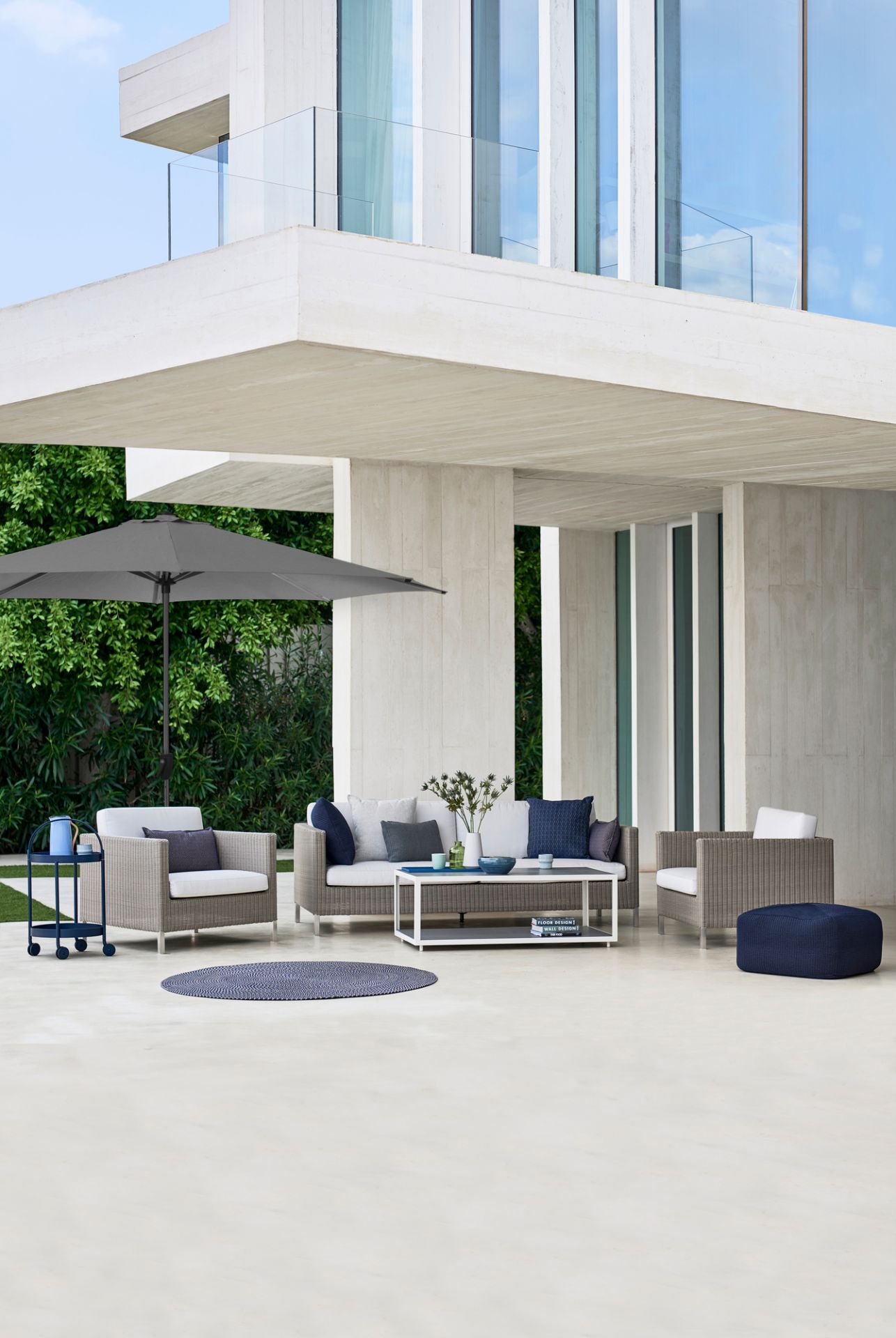 Grauer Sonnenschirm mit Cane-Line Sonnenschirmfuß im modernen Outdoor-Lounge-Bereich. Keywords: Sonnenschutz, Gartenmöbel, Design.