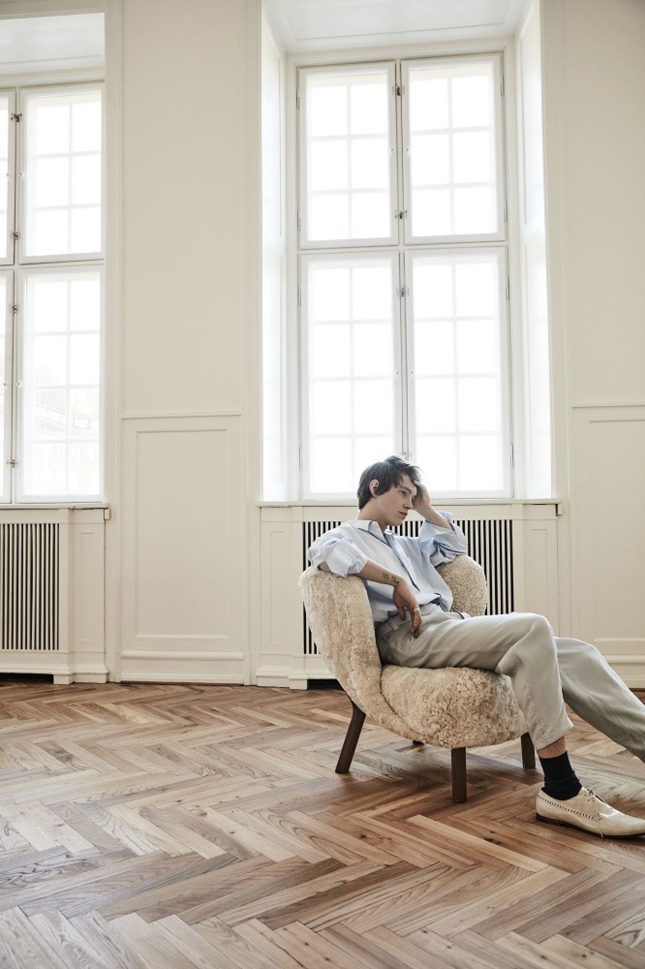 Mann sitzt entspannt im Little Petra Sessel von Andtradition, Eiche weiß mit Sahara-Bezug.