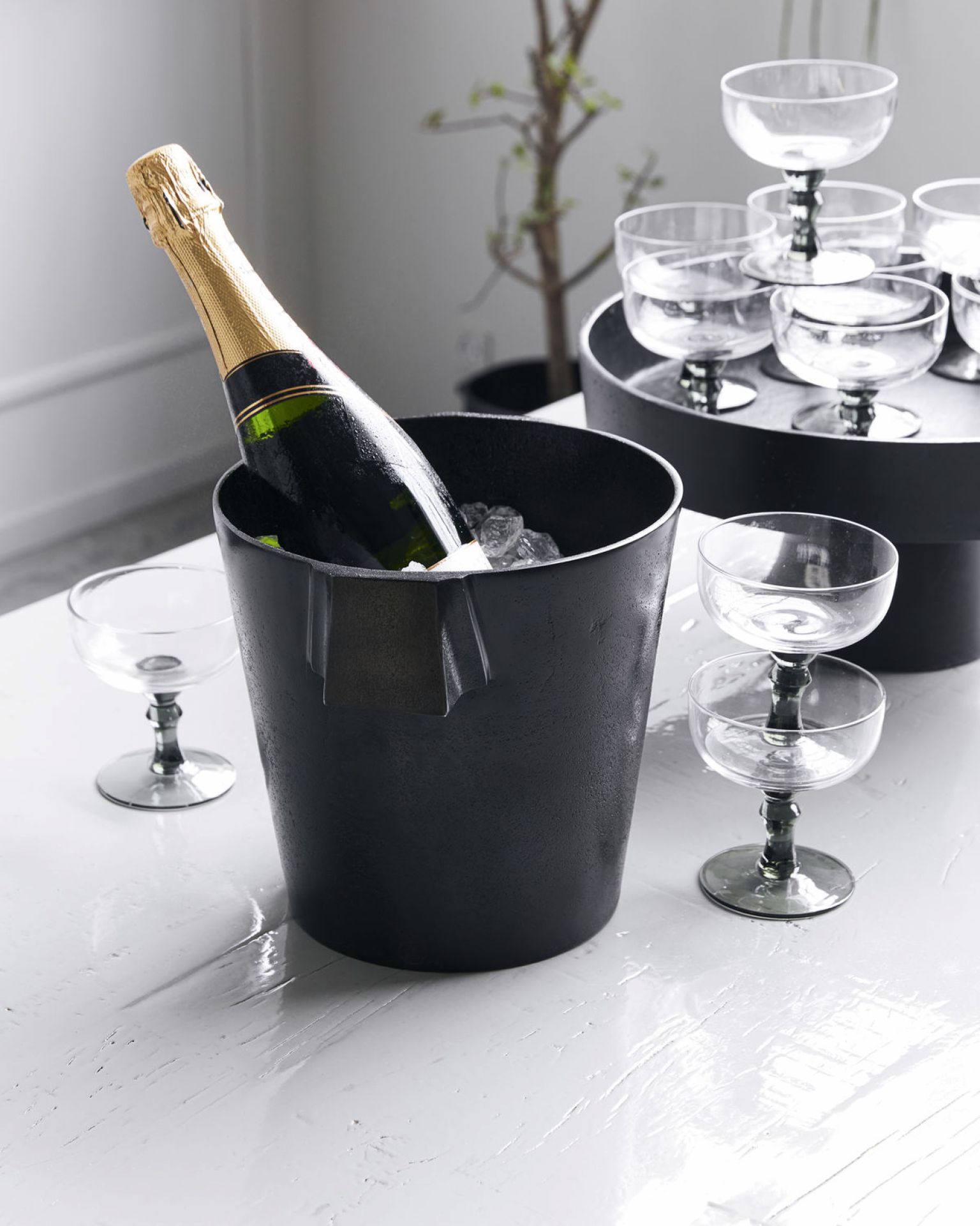 Schwarzer Buck Weinkühler von House Doctor mit Champagnerflasche und Eiswürfeln, daneben Cocktailgläser.