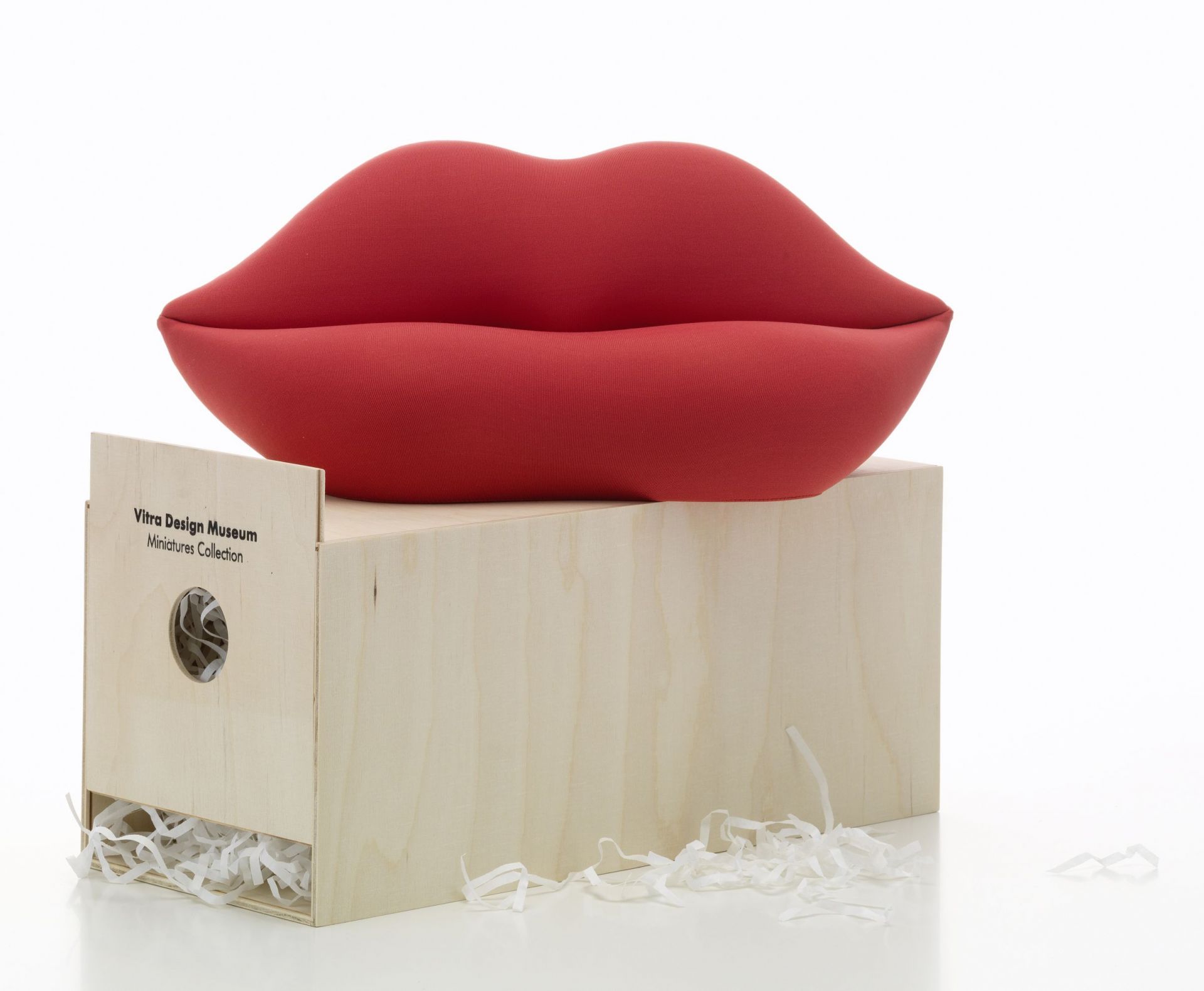 Rotes Bocca Sofa in Miniatur von Vitra auf einer Holzkiste mit Füllmaterial.