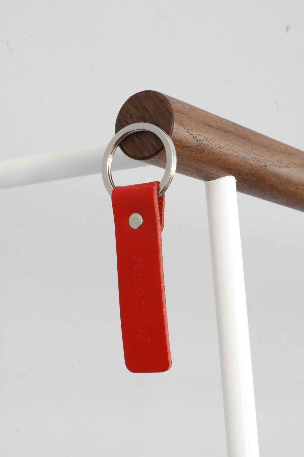 Detailaufnahme: Leanon II Anlehngarderobe mit Nussbaumstange, weißem Gestell und rotem Roomsafari Schlüsselanhänger.