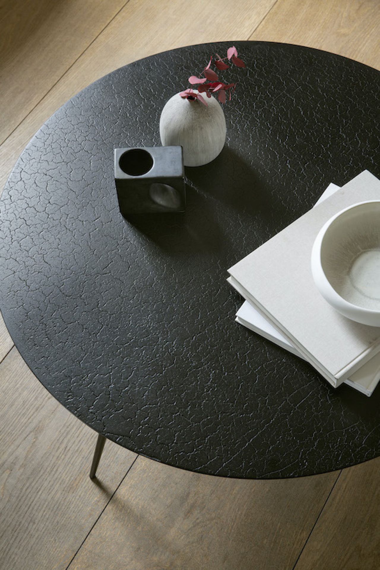 Runder, schwarzer Couchtisch mit Lava-Textur (Ethnicraft Luna) und Deko-Elementen auf Holzboden.