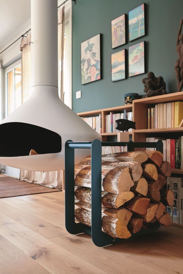 Nevado Holztrage von Fermob, gefüllt mit Brennholz, vor einem modernen Kamin und Bücherregal.