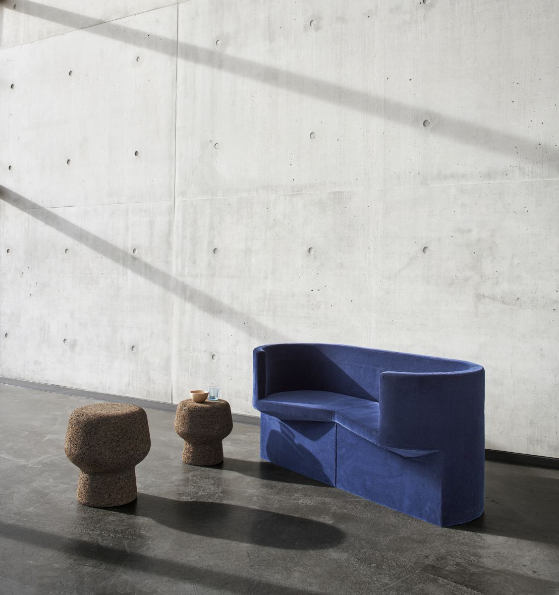 Corker Hocker von ClassiCon, zwei Korkhocker als Beistelltisch, blaue Bank vor Betonwand.