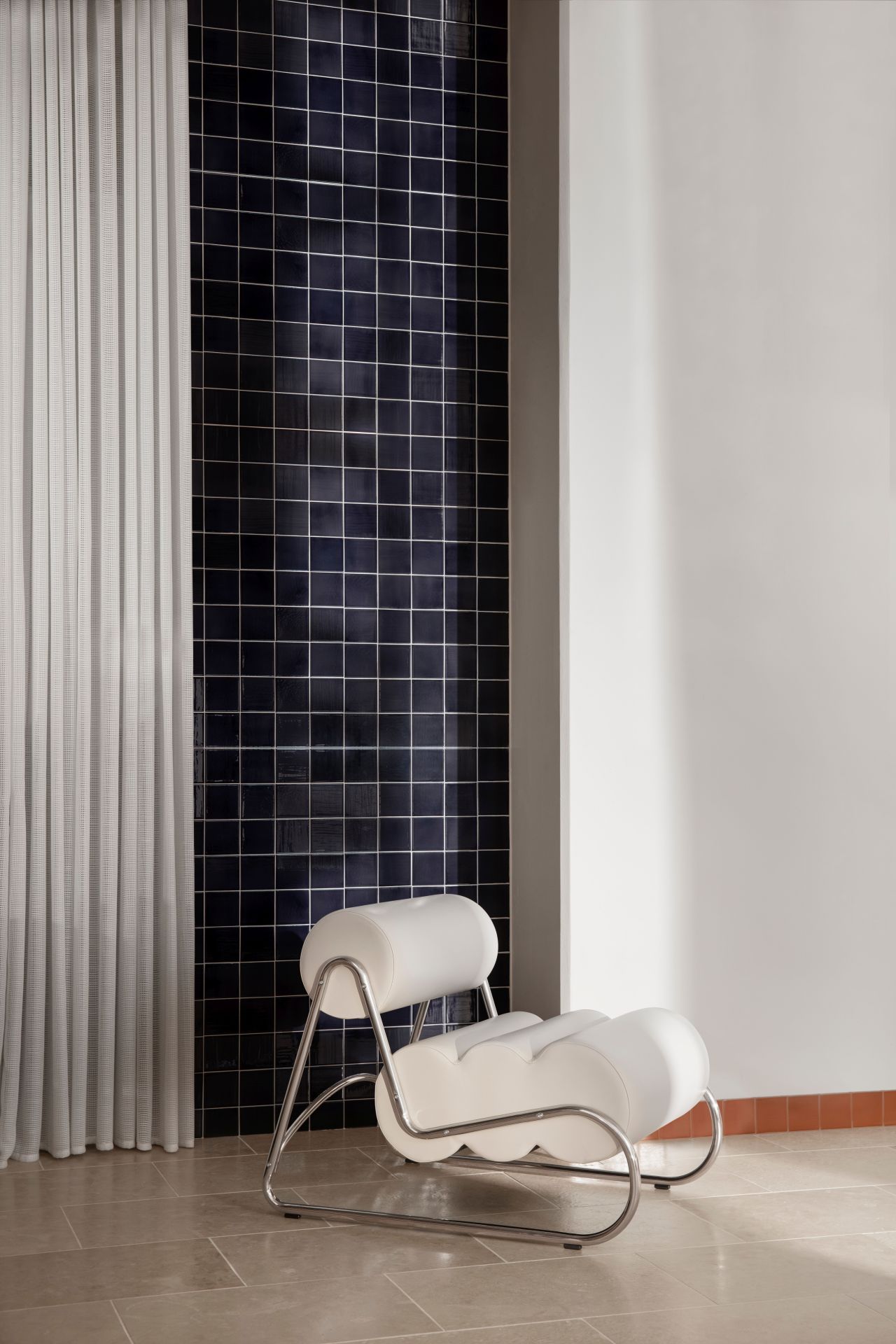 Weißer Fave Armchair Sessel von NORR11 mit Chromgestell vor dunkler Kachelwand und Vorhang.