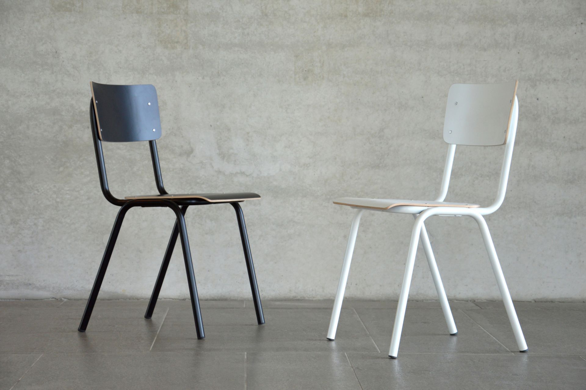 Zwei Jan Kurtz Zero Stühle, einer schwarz, einer weiß, vor einer Betonwand.