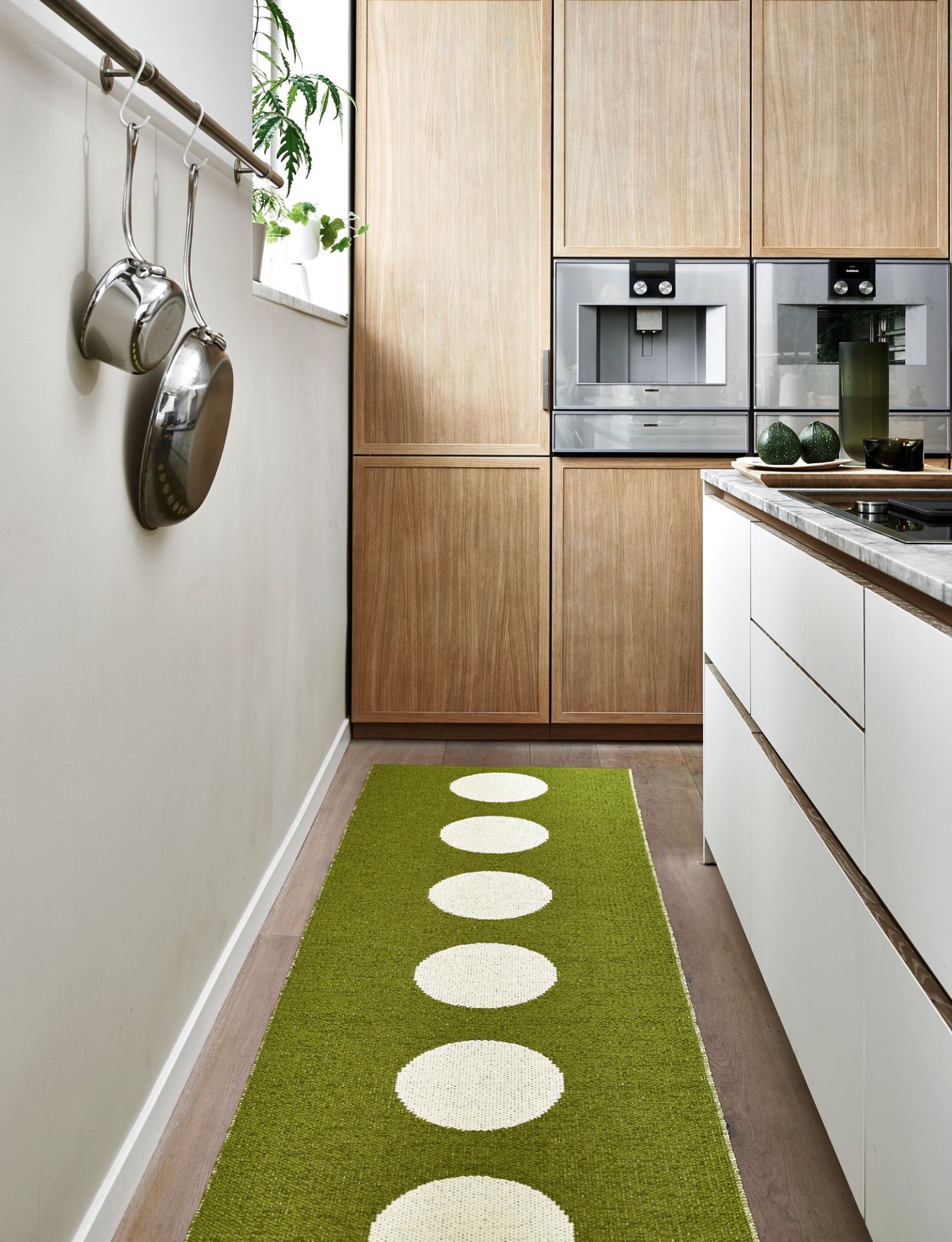 Vera Kunststoffteppich von Pappelina, 70x300 cm, in grüner Farbe mit weißen Kreisen im Küchenbereich.