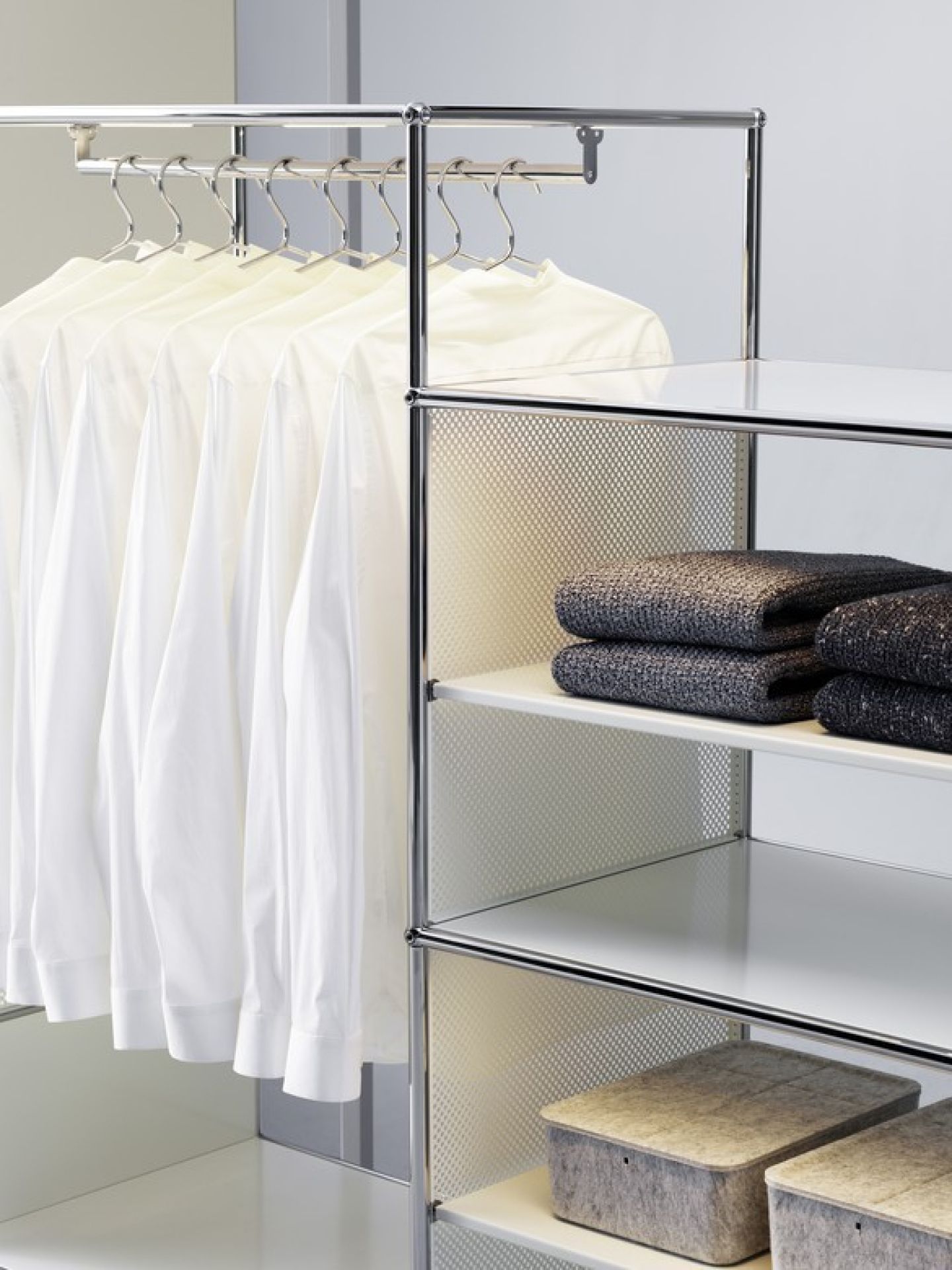 Detailaufnahme eines USM Haller Regalsystems mit Glasböden, Kleiderstange und Textilien.