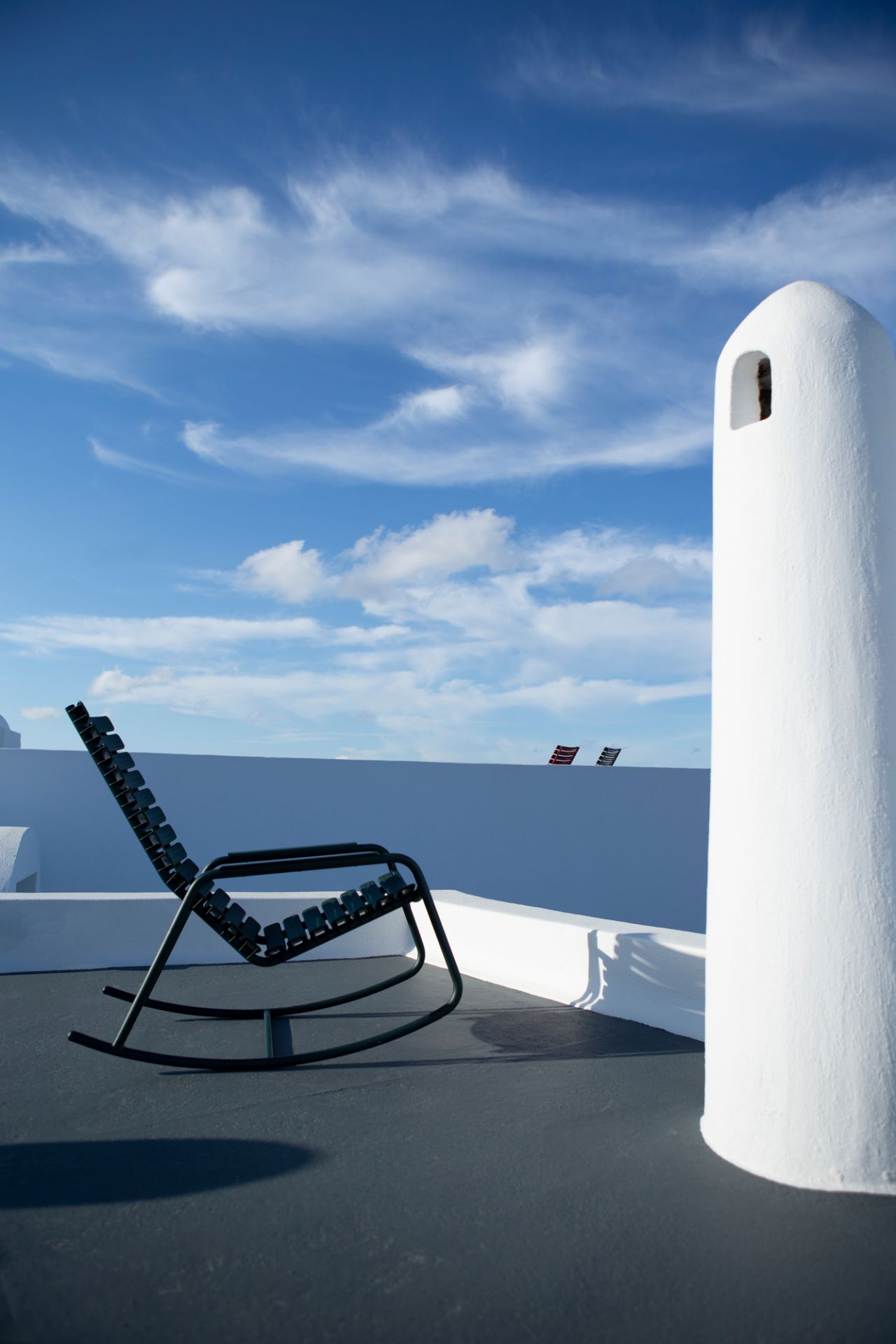 Houe ReClips Schaukelstuhl für den Außenbereich vor blauem Himmel und weißer Architektur.