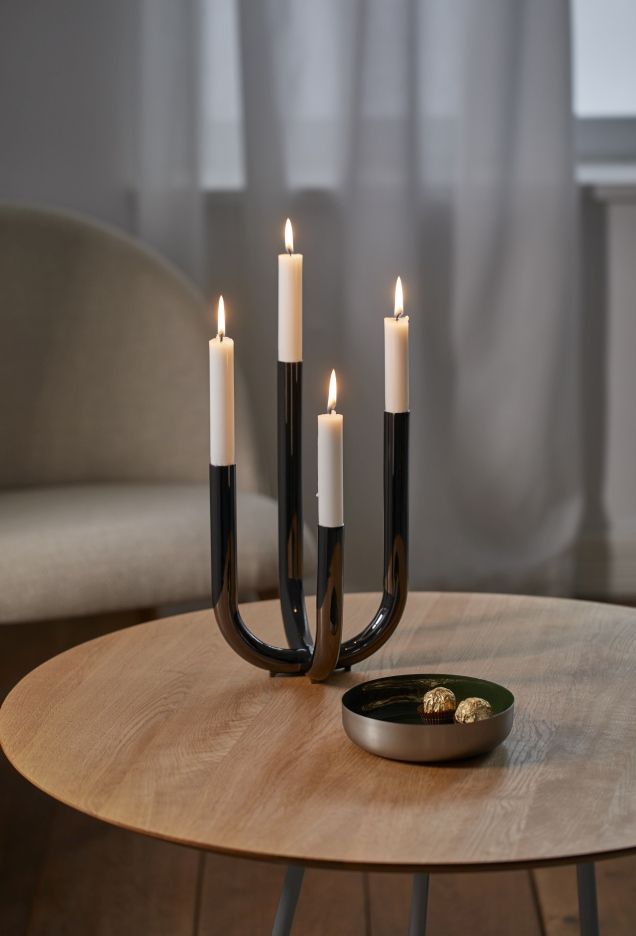 Philippi Festive Leuchter mit vier brennenden, weißen Kerzen auf einem Holztisch. Dekorative Beleuchtung.