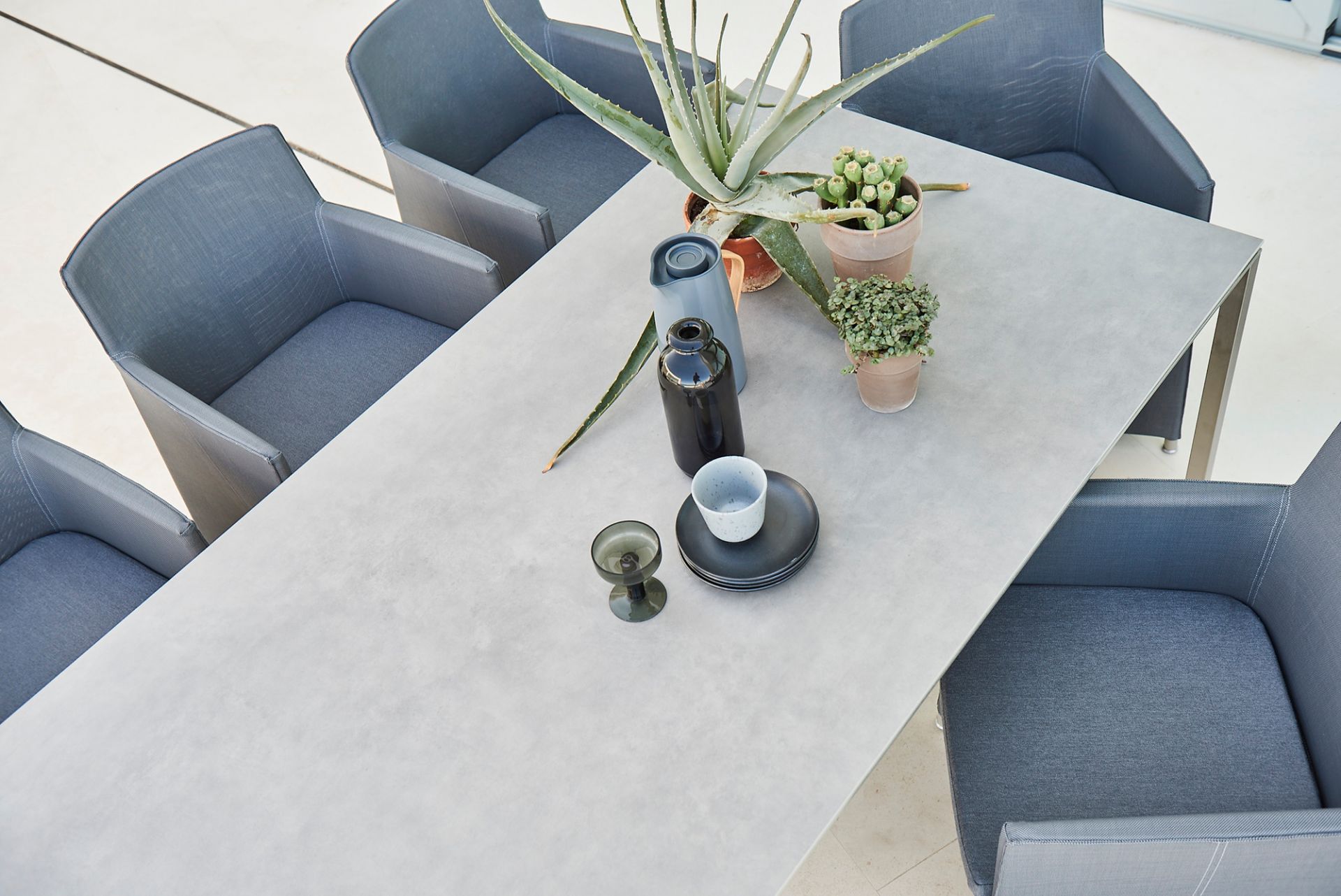 Cane-Line Pure Outdoor Esstisch, groß, betongrau, mit hellgrauen Stühlen und Dekoration von oben.