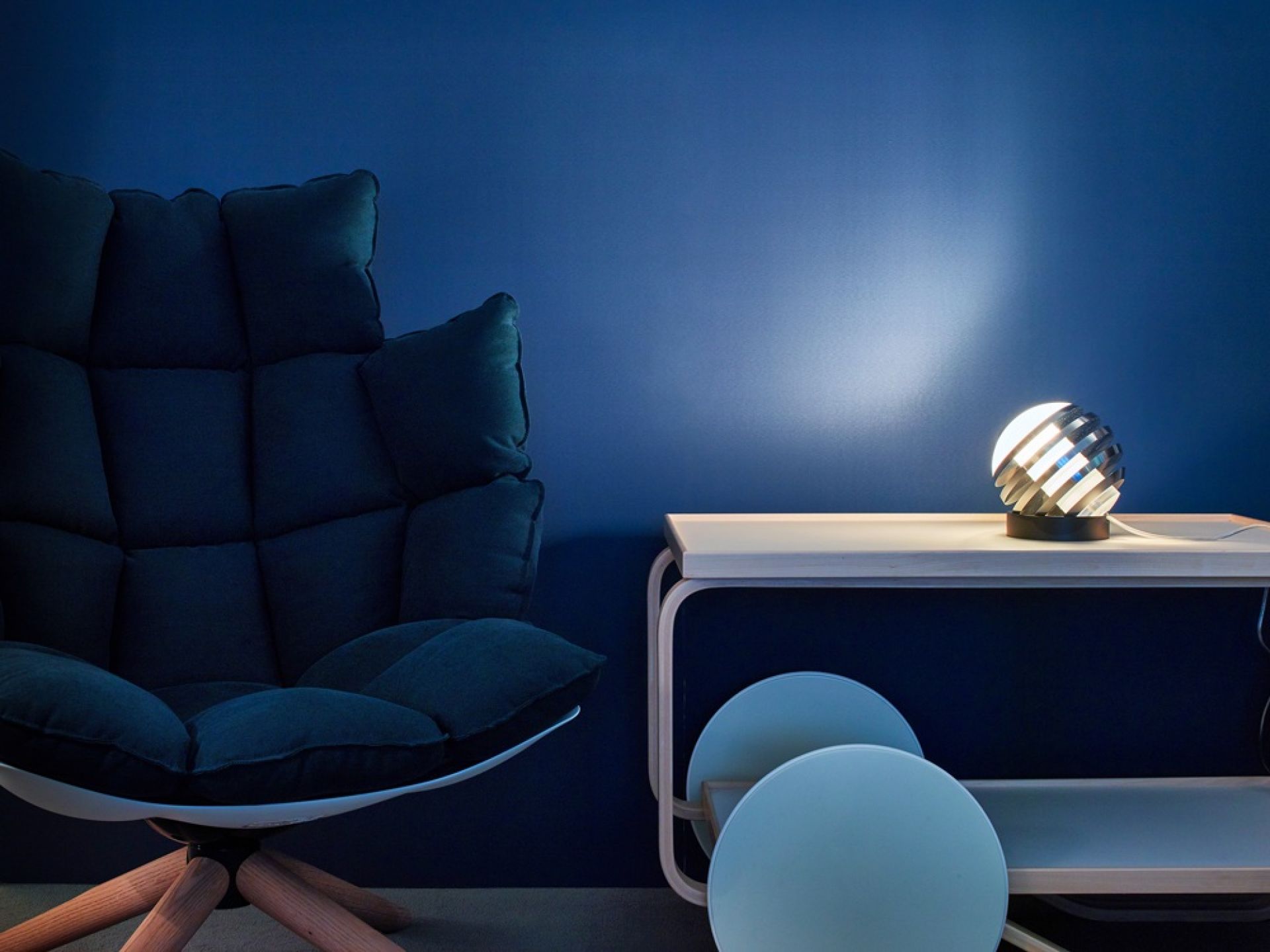 Bulo Tischleuchte Tecnolumen auf Tisch, neben Sessel vor blauer Wand. Design Lampe.