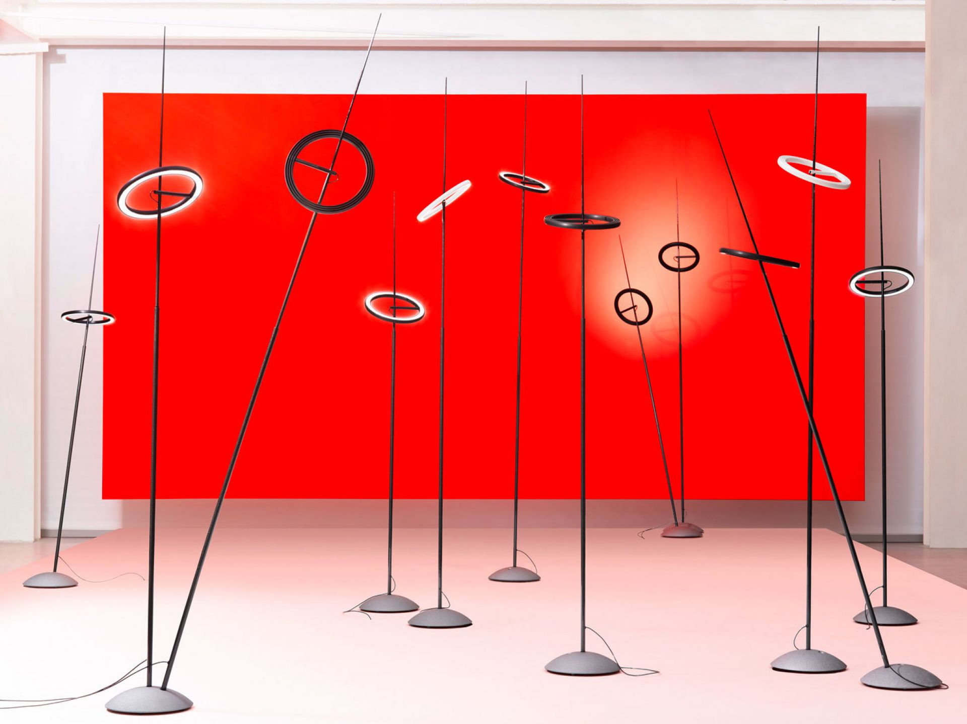 Mehrere schwarze Ringelpiez Stehlampen von Ingo Maurer vor rotem Hintergrund. Moderne Designleuchten für Wohnraum und Büro.