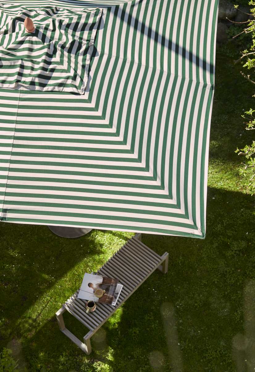 Messina Sonnenschirm mit dunkelblauen Streifen, Ø 270 cm, spendet Schatten über einer Gartenliege.