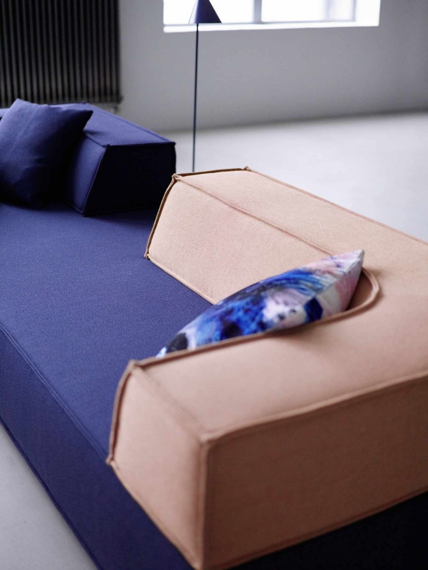 Detailaufnahme eines modularen Cor Trio Sofas mit blauen Sitzelementen und beigem Eckrücken mit dekorativem Kissen.