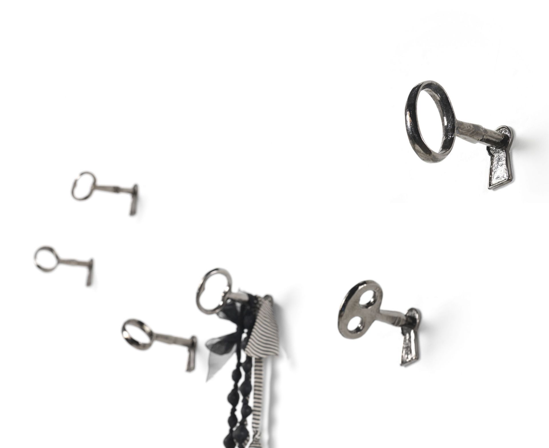 Mogg Memorie Wandhaken 4er Set: Schlüssel-förmige Wandhaken aus Metall an einer weißen Wand.