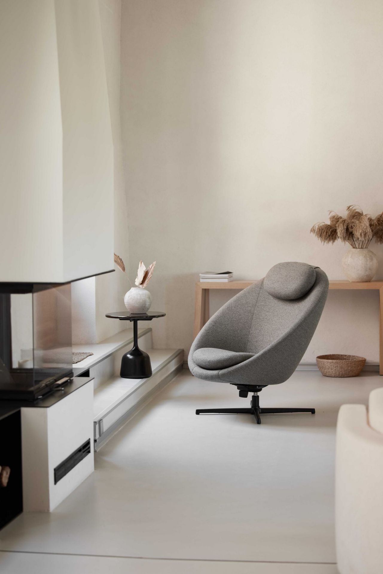 Grauer Cane-Line Pace Loungesessel mit Kopfstütze und schwarzem Drehfuß in modernem Wohnzimmer.