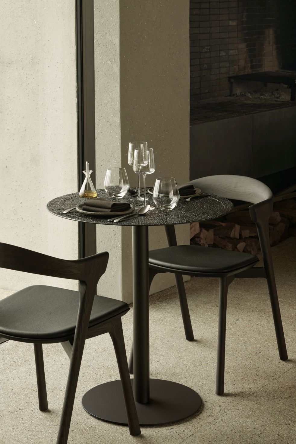 Blend Tisch Ø70cm von Ethnicraft in dunkler Bronze mit Stühlen und gedecktem Tisch für zwei Personen.