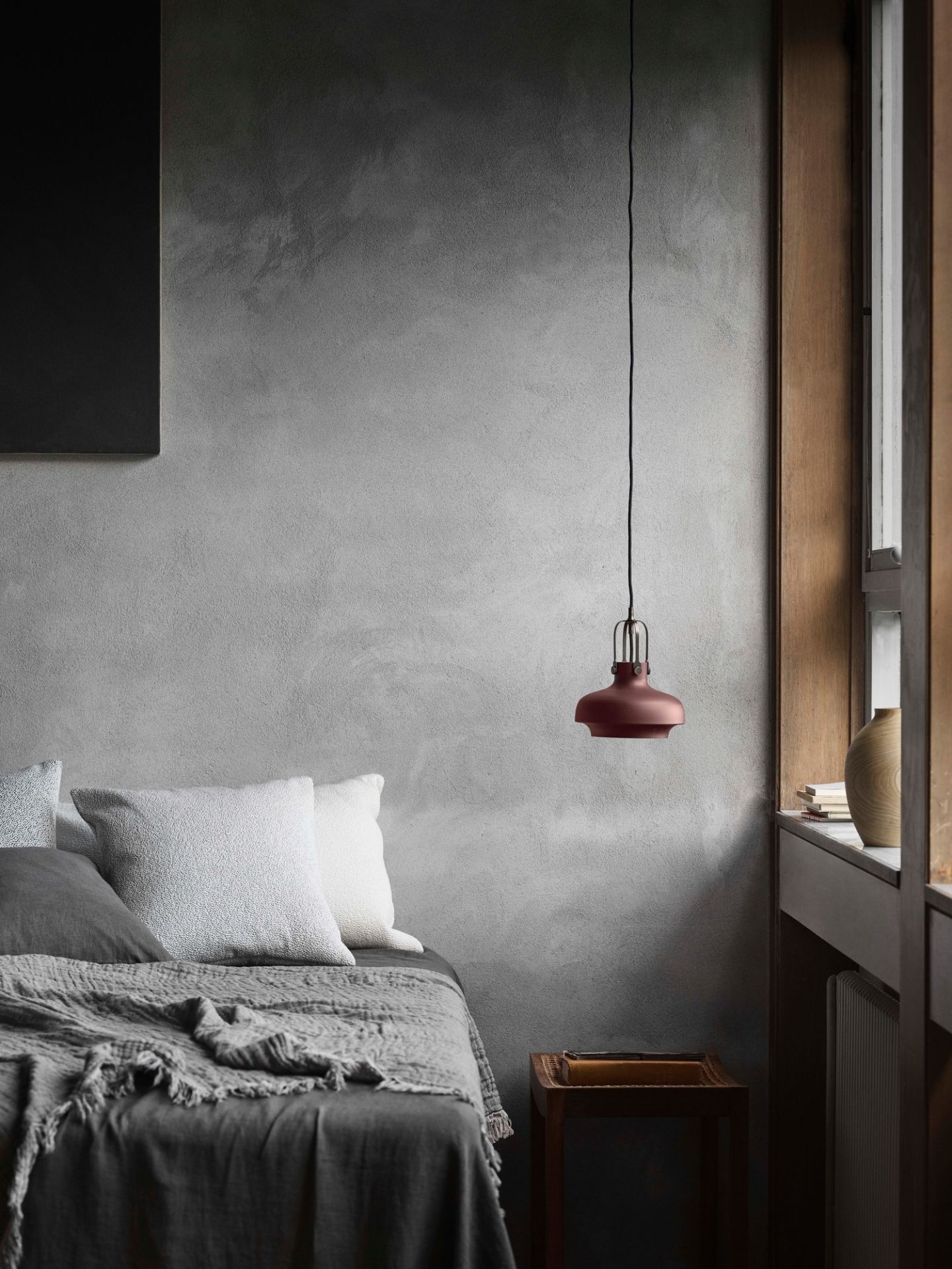 Nahaufnahme einer roten AndTradition Copenhagen Pendelleuchte über einem Bett in einem modernem Schlafzimmer.