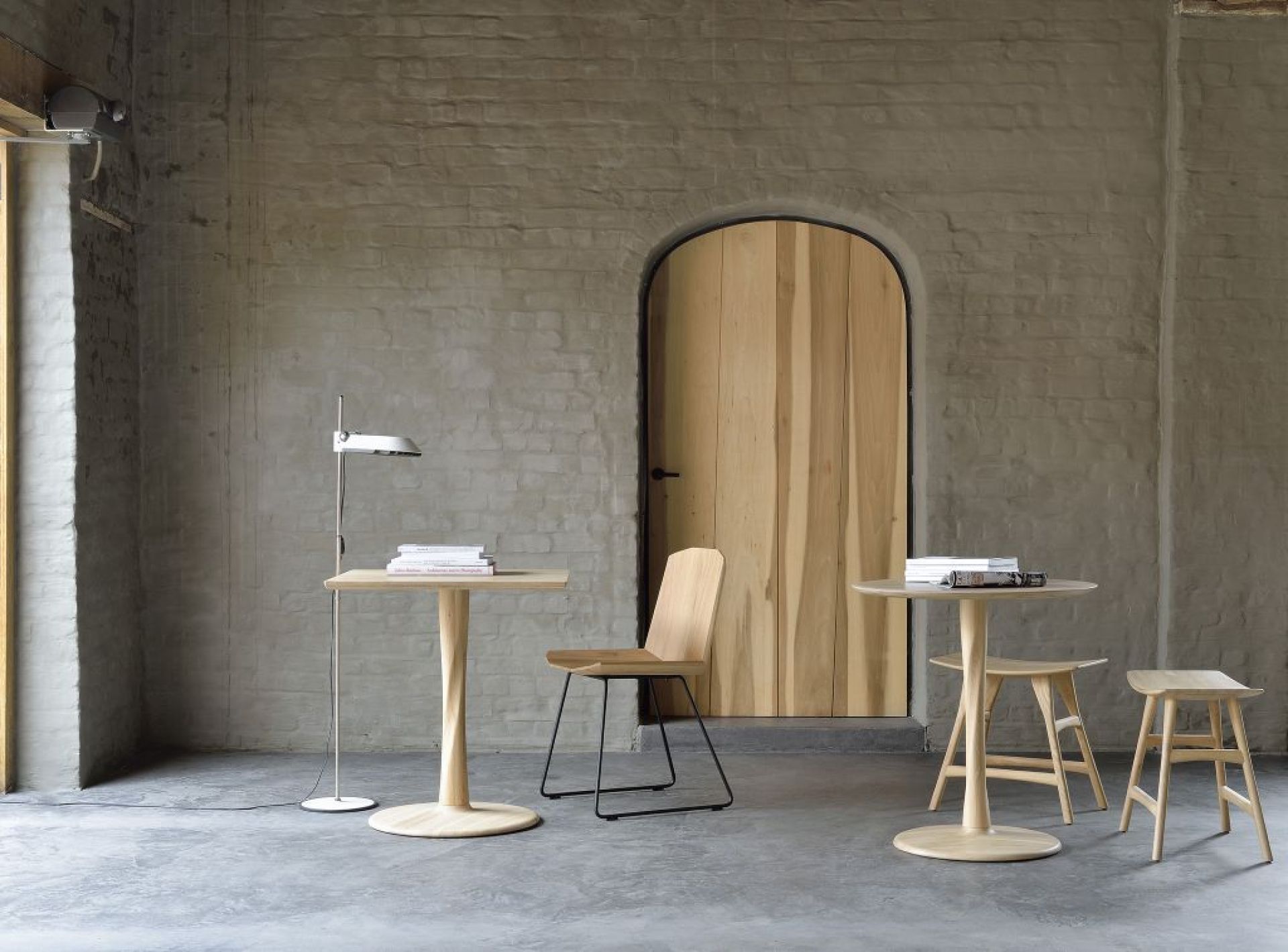 Ethnicraft Torsion Eiche Tisch und Stühle vor einer Holztür und grauer Ziegelwand.