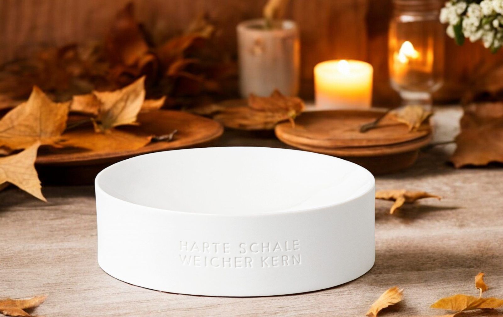 Weiße Räder Schale "Harte Schale weicher Kern" als Deko-Element mit Herbstlaub und Kerzen.