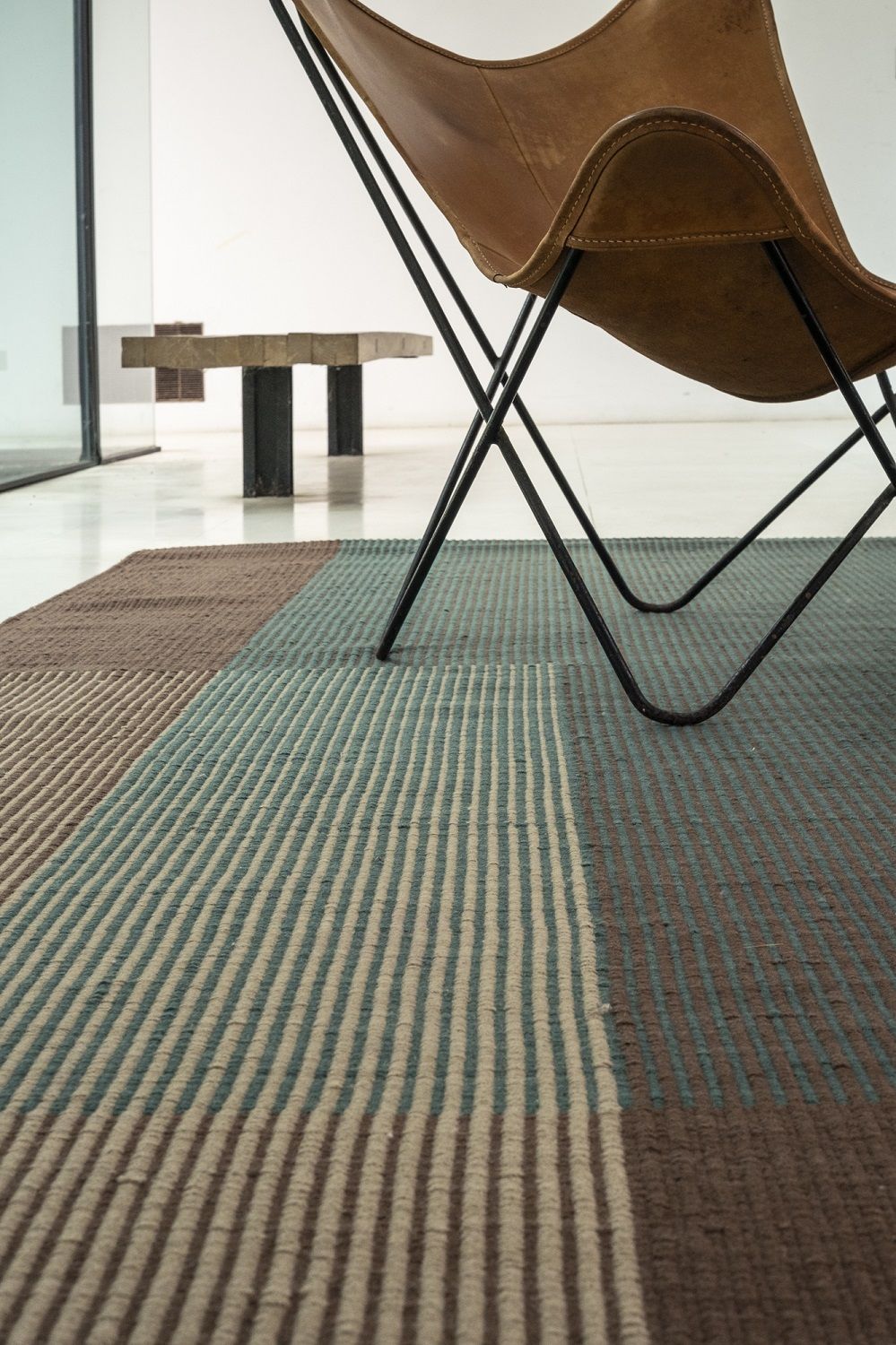 Detailaufnahme des Haze Rug Teppichs von Nanimarquina in Braun- und Blautönen unter einem Sessel.