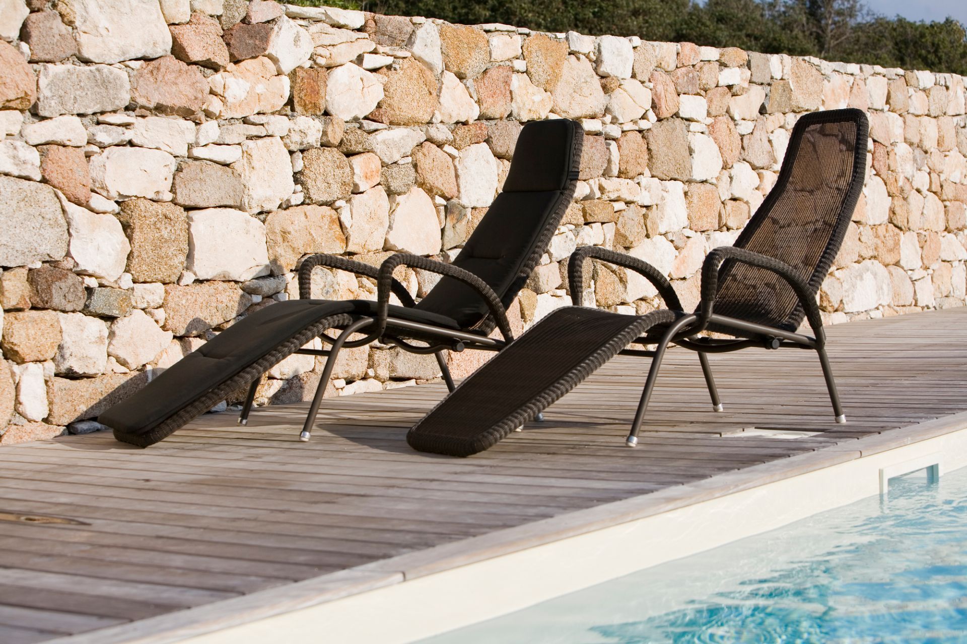 Zwei schwarze Cane-Line Sonnenliegen aus Rattan am Pool auf einer Holzterrasse.