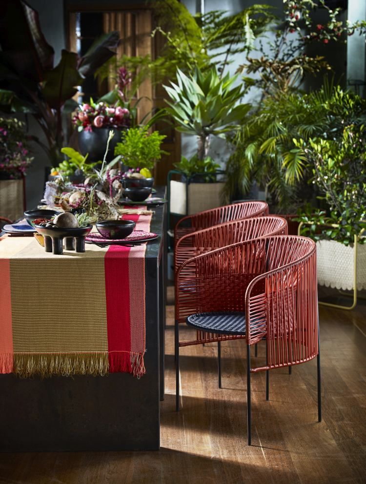 Caribe Chic Dining Chair: Outdoor Stuhl in Kupfer mit schwarzem Sitz vor üppigem Grün.