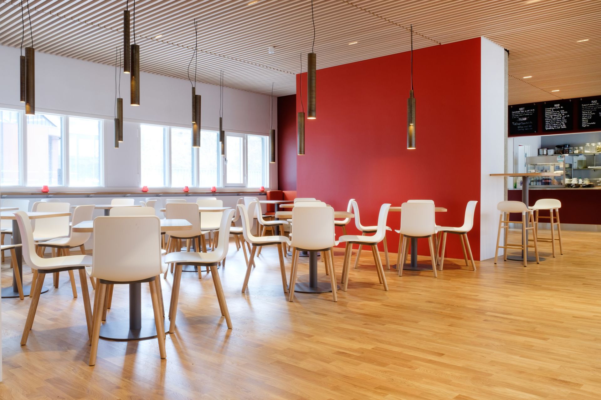 Innenaufnahme mit vielen weißen Hal Ply Wood Stühlen von Vitra an Tischen in einem Restaurant.