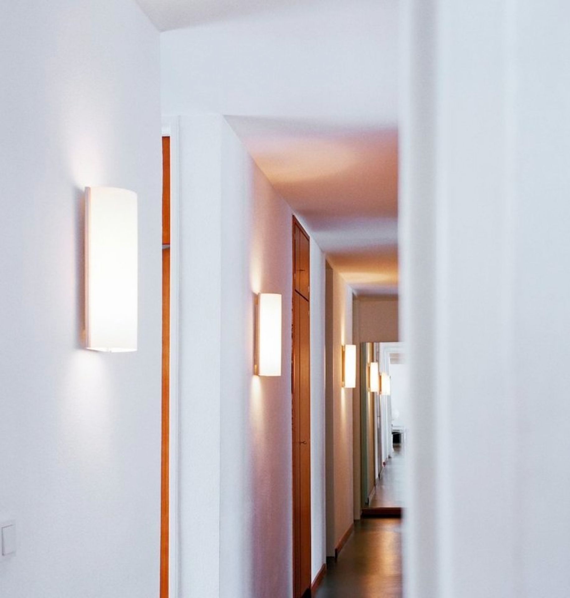 Flur mit mehreren leuchtenden, rechteckigen Club Wandleuchten von Serien Lighting an weißen Wänden.