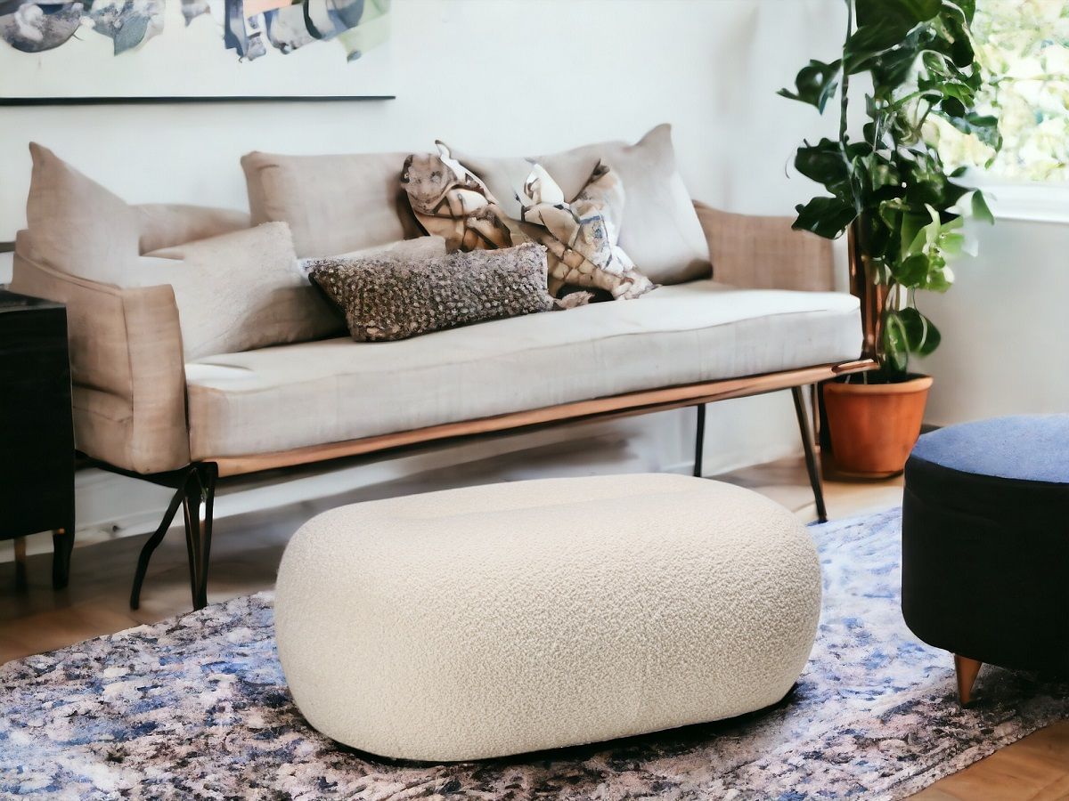 Beiger Nana Pouf Hocker von Freifrau Manufaktur im Wohnzimmer auf einem gemusterten Teppich.