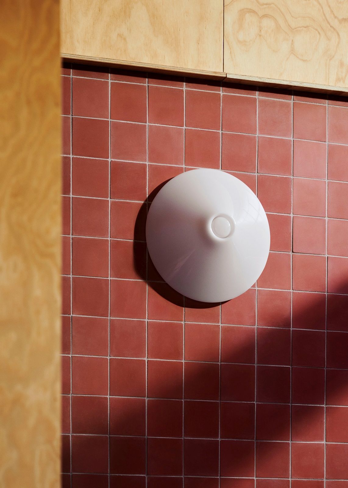 Weiße Ono Wandleuchte von Hay an roter Fliesenwand, modernes Design für Innenräume.