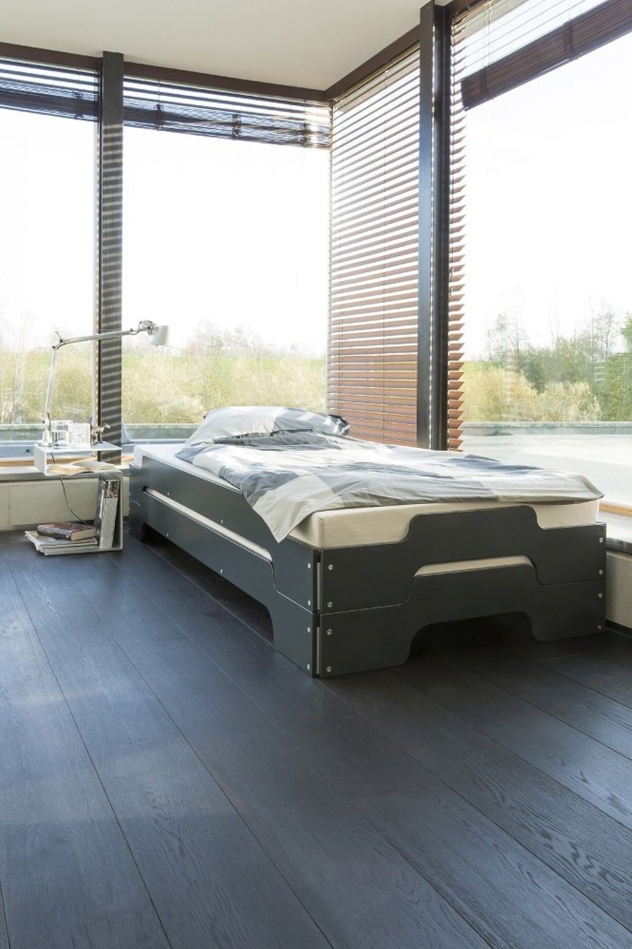 Graue Stapelliege Klassik von Müller Möbelwerkstätten vor Fenster mit Jalousien und Nachttisch.