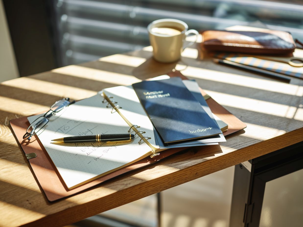 Detailaufnahme: Janua Hightable Tisch mit Bordbar, Notizbuch, Stift und Kaffeetasse im sonnigen Büro.
