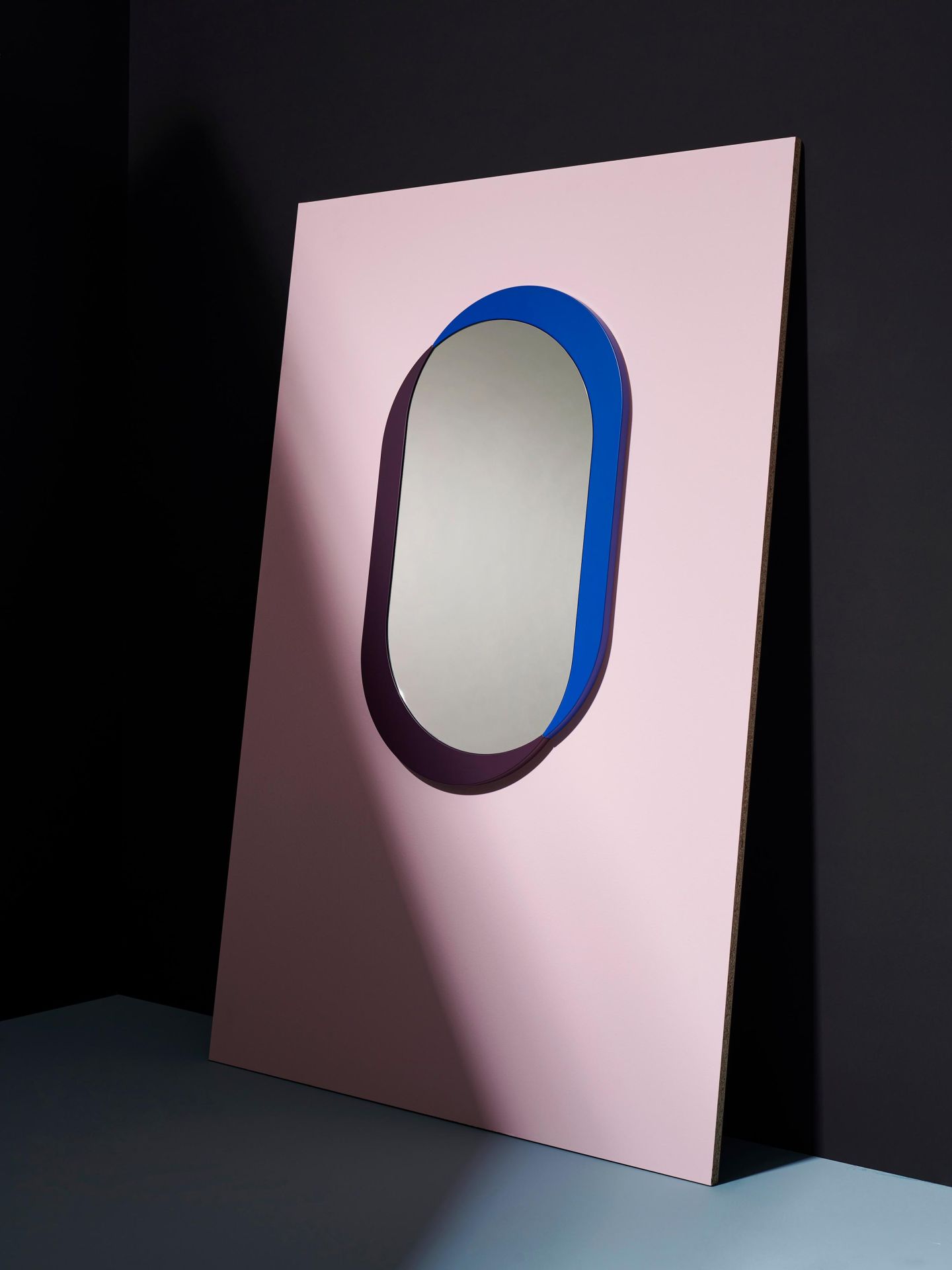 Kimo Wandspiegel M Schönbuch: Ovaler Spiegel mit blauem und lila Rahmen auf rosa Hintergrund.