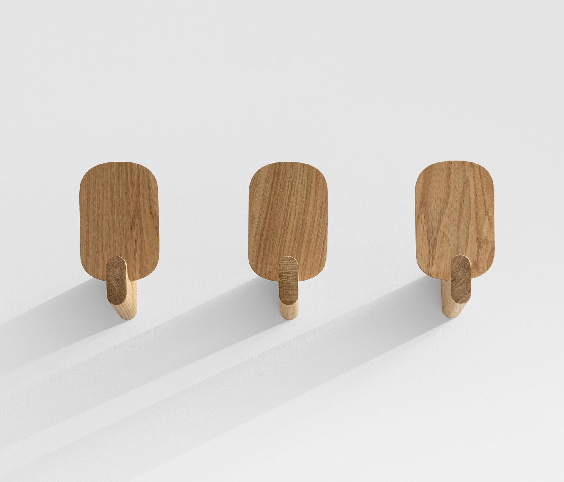 Drei Ad Hook Wandhaken aus Massivholz an einer weißen Wand, modernes Design.