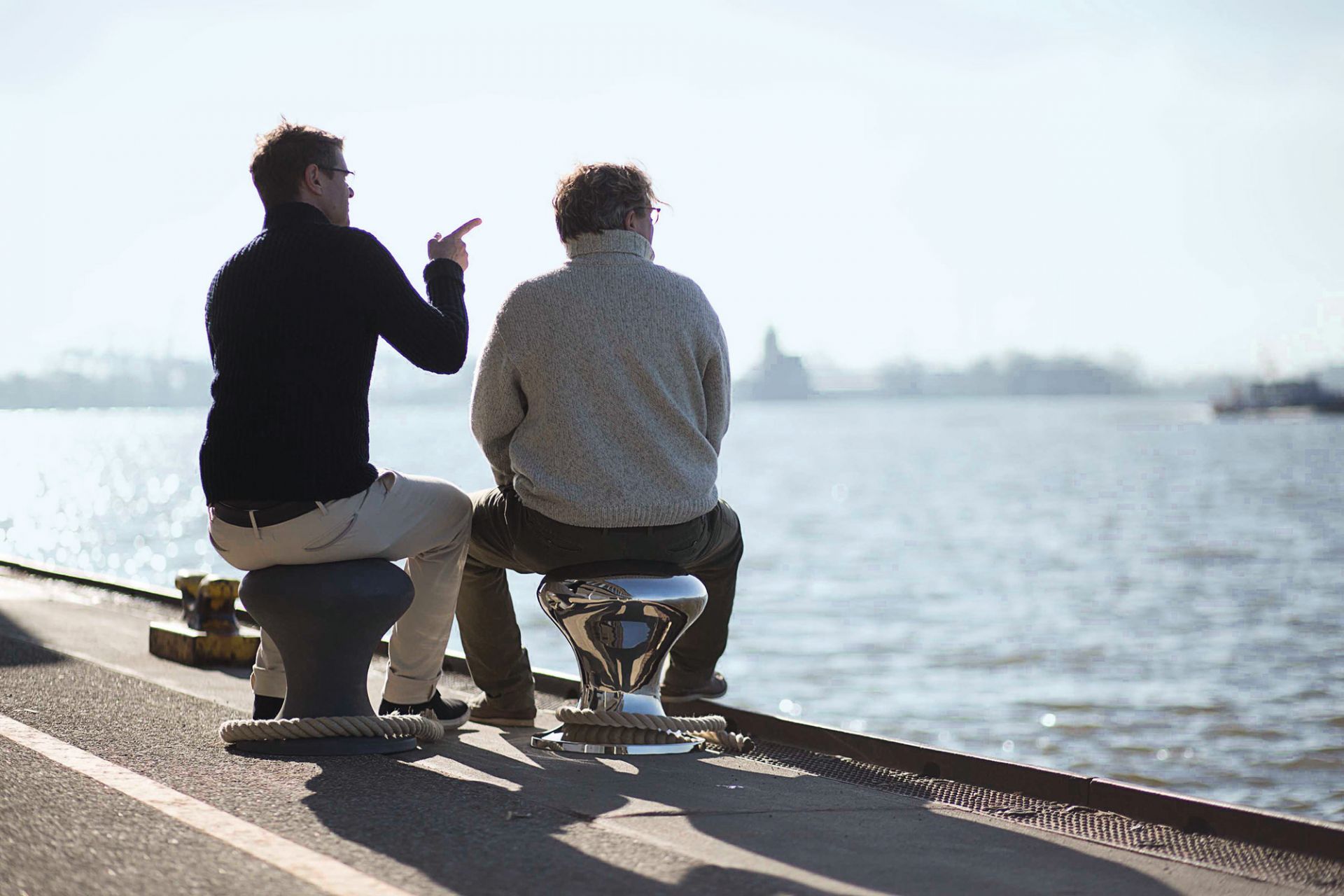 Zwei Männer sitzen auf Philippi Hockern am Wasser. Design Hocker für stilvolles Sitzen.