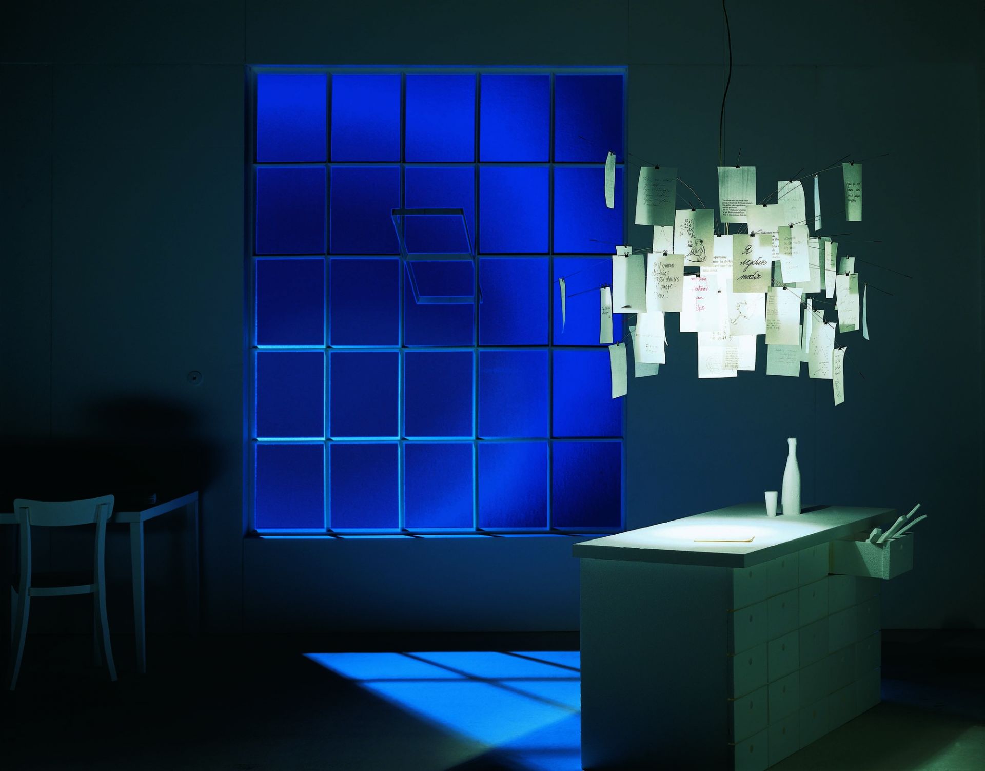 Ingo Maurer Zettel'z 5 Hängeleuchte mit Notizen im modernen Ambiente, blaues Fenster im Hintergrund.