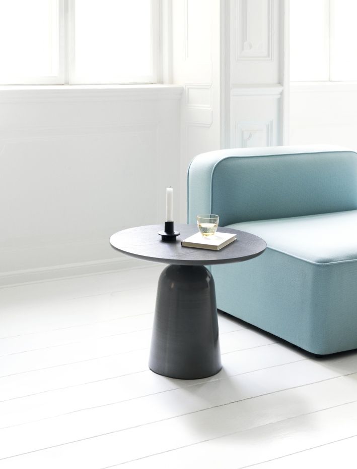 Normann Copenhagen Turn Table Tisch in Grau, mit Kerze, Buch und Glas auf weißem Holzboden.