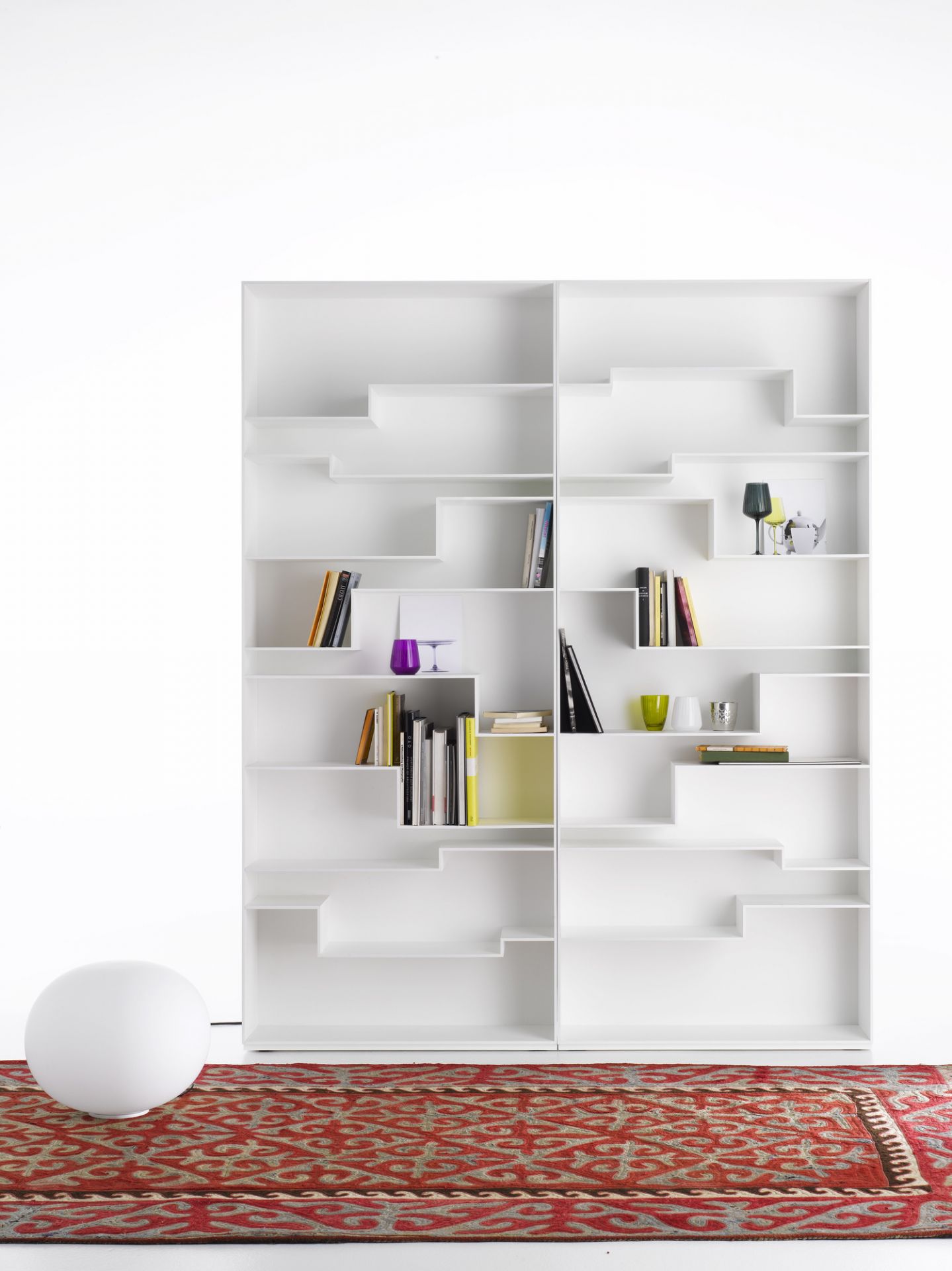 Weißes Melody Regalsystem von MDF Italia mit Büchern und Deko-Objekten auf einem gemusterten Teppich.